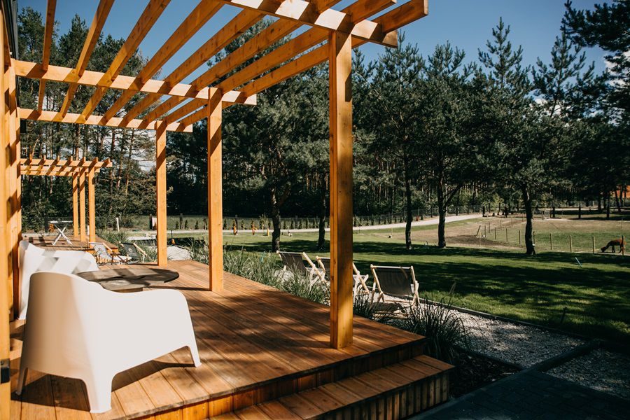 Drewniana pergola z leżakami na terenie Ceglanego Domu, otoczona sosnowym lasem