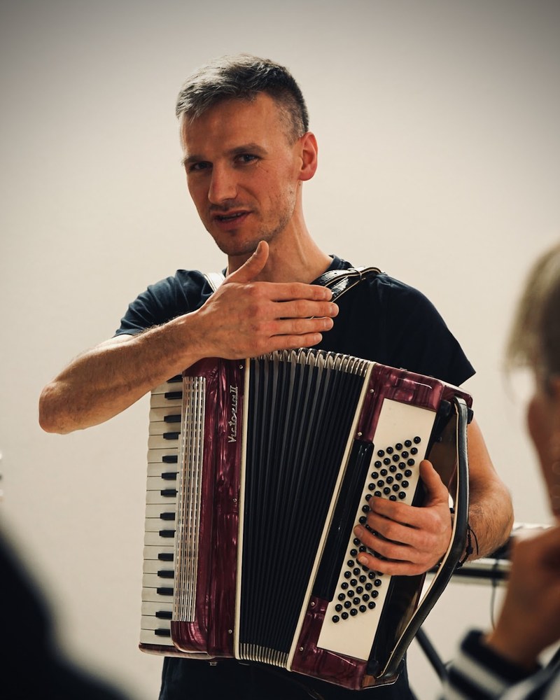 Adam Konieczny gra na akordeonie, gestykulując do słuchaczy podczas warsztatów muzycznych
